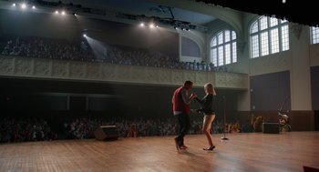 Movie still from “Pitch Perfect 2” (2015), directed by Elizabeth Banks – A couple of people on a stage with a microphone; Extreme Wide shot, High angle