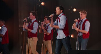 Movie still from “Pitch Perfect 2” (2015), directed by Elizabeth Banks – A group of men singing into microphones on a stage; Medium shot, Over the shoulder angle