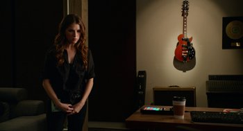 Movie still from “Pitch Perfect 2” (2015), directed by Elizabeth Banks – A beautiful young woman standing next to a table; Medium shot, Over the shoulder angle