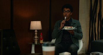 Movie still from “Pitch Perfect 2” (2015), directed by Elizabeth Banks – A man sitting in front of a plate of cake; Medium shot, Over the shoulder angle