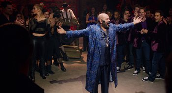 Movie still from “Pitch Perfect 2” (2015), directed by Elizabeth Banks – A man with a beard and a blue robe is in front of a group of people; Wide shot, Low angle