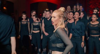 Movie still from “Pitch Perfect 2” (2015), directed by Elizabeth Banks – A group of people in black outfits singing in front of a crowd; Medium shot, Over the shoulder angle