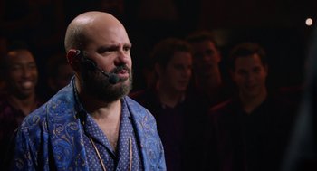Movie still from “Pitch Perfect 2” (2015), directed by Elizabeth Banks – A man with a beard is wearing a blue robe; Close Up shot, Over the shoulder angle