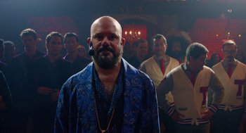 Movie still from “Pitch Perfect 2” (2015), directed by Elizabeth Banks – A man with a bald head wearing a blue robe; Medium shot, Low angle