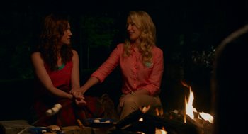 Movie still from “Pitch Perfect 2” (2015), directed by Elizabeth Banks – Two women sitting in front of a fire holding hands; Medium shot, Over the shoulder angle