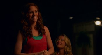 Movie still from “Pitch Perfect 2” (2015), directed by Elizabeth Banks – Two young women smiling for the camera in the dark; Medium shot, Over the shoulder angle