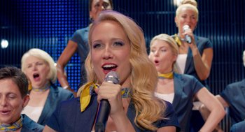 Movie still from “Pitch Perfect 2” (2015), directed by Elizabeth Banks – A woman singing into a microphone with other women in the background; Close Up shot, Overhead angle
