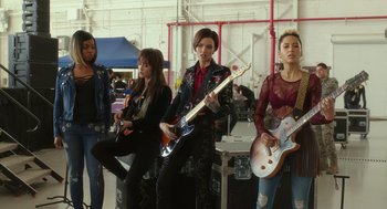 Movie still from “Pitch Perfect 3” (2017), directed by Trish Sie – A group of young people holding guitars in a room; Wide shot, Low angle
