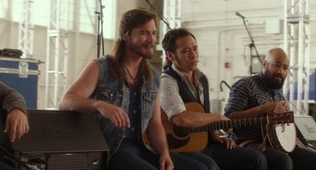 Movie still from “Pitch Perfect 3” (2017), directed by Trish Sie – A man sitting next to another man holding a guitar; Medium shot, Over the shoulder angle