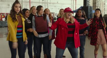 Movie still from “Pitch Perfect 3” (2017), directed by Trish Sie – A group of women standing in a room singing together; Medium shot, Over the shoulder angle