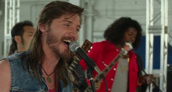 Movie still from “Pitch Perfect 3” (2017), directed by Trish Sie – A man with long hair is singing into a microphone; Close Up shot, Over the shoulder angle