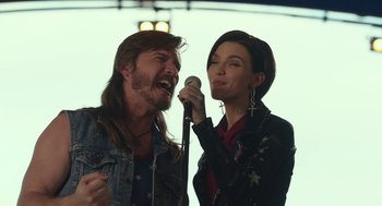 Movie still from “Pitch Perfect 3” (2017), directed by Trish Sie – A man and a woman sing into a microphone; Medium shot, Over the shoulder angle