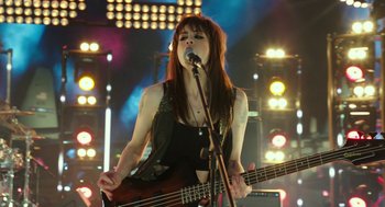 Movie still from “Pitch Perfect 3” (2017), directed by Trish Sie – A woman holding a guitar and singing into a microphone; Medium shot, Low angle