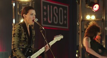 Movie still from “Pitch Perfect 3” (2017), directed by Trish Sie – A person with a microphone and a white guitar; Medium shot, Low angle