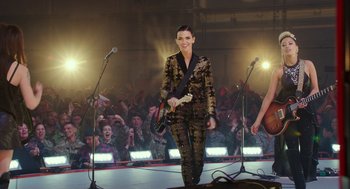 Movie still from “Pitch Perfect 3” (2017), directed by Trish Sie – A woman in a black and gold outfit holding a guitar; Wide shot, Over the shoulder angle