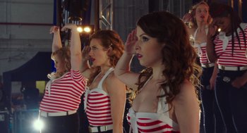 Movie still from “Pitch Perfect 3” (2017), directed by Trish Sie – A group of young women saluting in front of an audience; Medium shot, Low angle