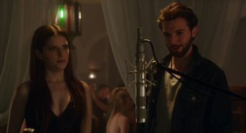 Movie still from “Pitch Perfect 3” (2017), directed by Trish Sie – A man and a woman standing in front of a microphone; Close Up shot, Over the shoulder angle