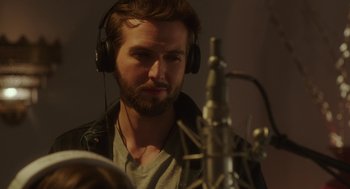 Movie still from “Pitch Perfect 3” (2017), directed by Trish Sie – A man with headphones is listening to music in front of a microphone; Close Up shot, Over the shoulder angle