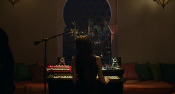 Movie still from “Pitch Perfect 3” (2017), directed by Trish Sie – A woman sitting in front of a keyboard in front of a microphone; Wide shot, High angle