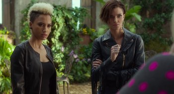 Movie still from “Pitch Perfect 3” (2017), directed by Trish Sie – A couple of women standing next to each other in a garden; Medium shot, Over the shoulder angle