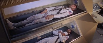 Movie still from “Planet of the Apes” (1968), directed by Franklin J. Schaffner – Two men in white suits laying down on a bed; Wide shot, Overhead angle