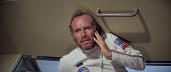 Movie still from “Planet of the Apes” (1968), directed by Franklin J. Schaffner – A man in a spacesuit holding his hand up to his face; Close Up shot, Overhead angle