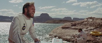 Movie still from “Planet of the Apes” (1968), directed by Franklin J. Schaffner – A man smiles while sitting on a boat in the water; Medium shot, Low angle