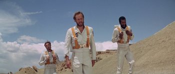 Movie still from “Planet of the Apes” (1968), directed by Franklin J. Schaffner – A group of men in white suits standing on top of a dirt hill; Medium shot, Low angle