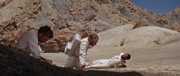 Movie still from “Planet of the Apes” (1968), directed by Franklin J. Schaffner – Two men in white suits are laying on the ground; Wide shot, High angle