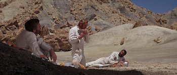 Movie still from “Planet of the Apes” (1968), directed by Franklin J. Schaffner – Two men in white are sitting on the ground; Wide shot, High angle