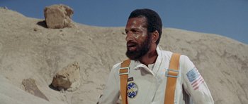 Movie still from “Planet of the Apes” (1968), directed by Franklin J. Schaffner – A man with a beard wearing a white shirt and orange suspenders; Medium shot, Low angle