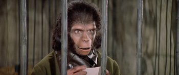 Movie still from “Planet of the Apes” (1968), directed by Franklin J. Schaffner – A man in a gorilla suit holding a piece of paper in a cage; Close Up shot, High angle