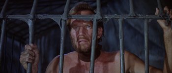 Movie still from “Planet of the Apes” (1968), directed by Franklin J. Schaffner – A shirtless man behind bars looking at the camera; Close Up shot, Low angle