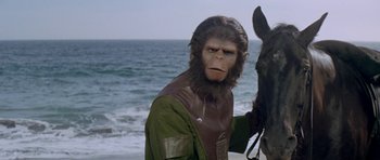 Movie still from “Planet of the Apes” (1968), directed by Franklin J. Schaffner – An image of a man dressed like a monkey with a horse on the beach; Close Up shot, Over the shoulder angle