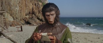 Movie still from “Planet of the Apes” (1968), directed by Franklin J. Schaffner – A man dressed as a monkey holding a piece of paper on the beach; Close Up shot, Low angle