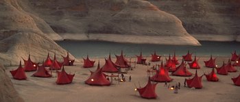 Movie still from “Planet of the Apes” (2001), directed by Tim Burton – A group of red tents in the sand near a body of water; Extreme Wide shot, High angle