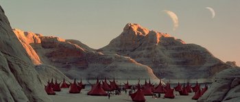 Movie still from “Planet of the Apes” (2001), directed by Tim Burton – A group of people standing in the sand next to tents; Extreme Wide shot, Low angle