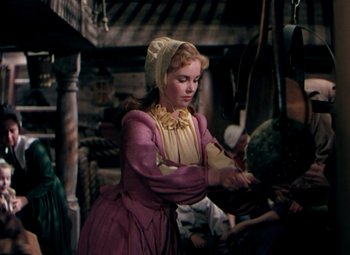 Movie still from “Plymouth Adventure” (1952), directed by Clarence Brown – A woman in a purple and yellow dress standing in a room; Medium shot, High angle