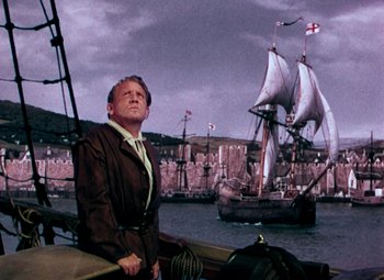 Movie still from “Plymouth Adventure” (1952), directed by Clarence Brown – A man standing on the side of a boat in front of a ship; Medium shot, Low angle
