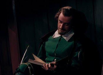 Movie still from “Plymouth Adventure” (1952), directed by Clarence Brown – A man sitting in a chair reading a book; Medium shot, High angle