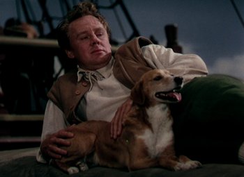 Movie still from “Plymouth Adventure” (1952), directed by Clarence Brown – A man sitting on a couch next to a brown dog; Medium shot, High angle