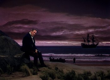 Movie still from “Plymouth Adventure” (1952), directed by Clarence Brown – A man sitting on top of a rock on the beach; Wide shot, Low angle
