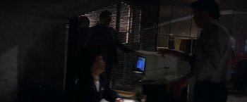 Movie still from “Point of No Return” (1993), directed by John Badham – A man in a black suit is sitting in front of a computer; Medium shot, Over the shoulder angle
