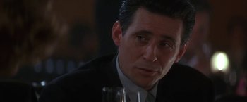 Movie still from “Point of No Return” (1993), directed by John Badham – A man in a suit and tie sitting at a table with a glass of wine; Close Up shot, Over the shoulder angle
