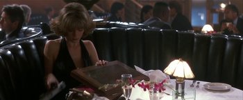 Movie still from “Point of No Return” (1993), directed by John Badham – A woman sitting at a table in front of a wooden box; Medium shot, Over the shoulder angle