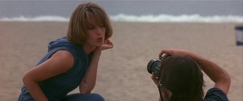 Movie still from “Point of No Return” (1993), directed by John Badham – A woman sitting on the beach taking a picture of another woman; Medium shot, Low angle