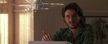 Movie still from “Point of No Return” (1993), directed by John Badham – A man sitting at a table writing on a piece of paper; Close Up shot, Low angle