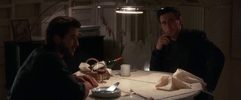 Movie still from “Point of No Return” (1993), directed by John Badham – Two men sitting at a dinner table with a bottle of wine; Medium shot, Over the shoulder angle