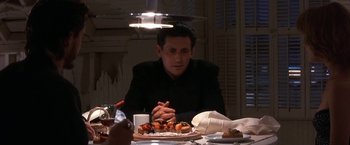 Movie still from “Point of No Return” (1993), directed by John Badham – A man sitting at a dinner table with a plate in front of him; Medium shot, Over the shoulder angle