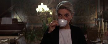 Movie still from “Point of No Return” (1993), directed by John Badham – A woman drinking from a white cup in a room; Medium shot, Low angle